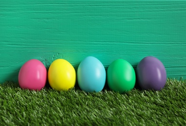 Photo of Bright Easter eggs on green grass against wooden background