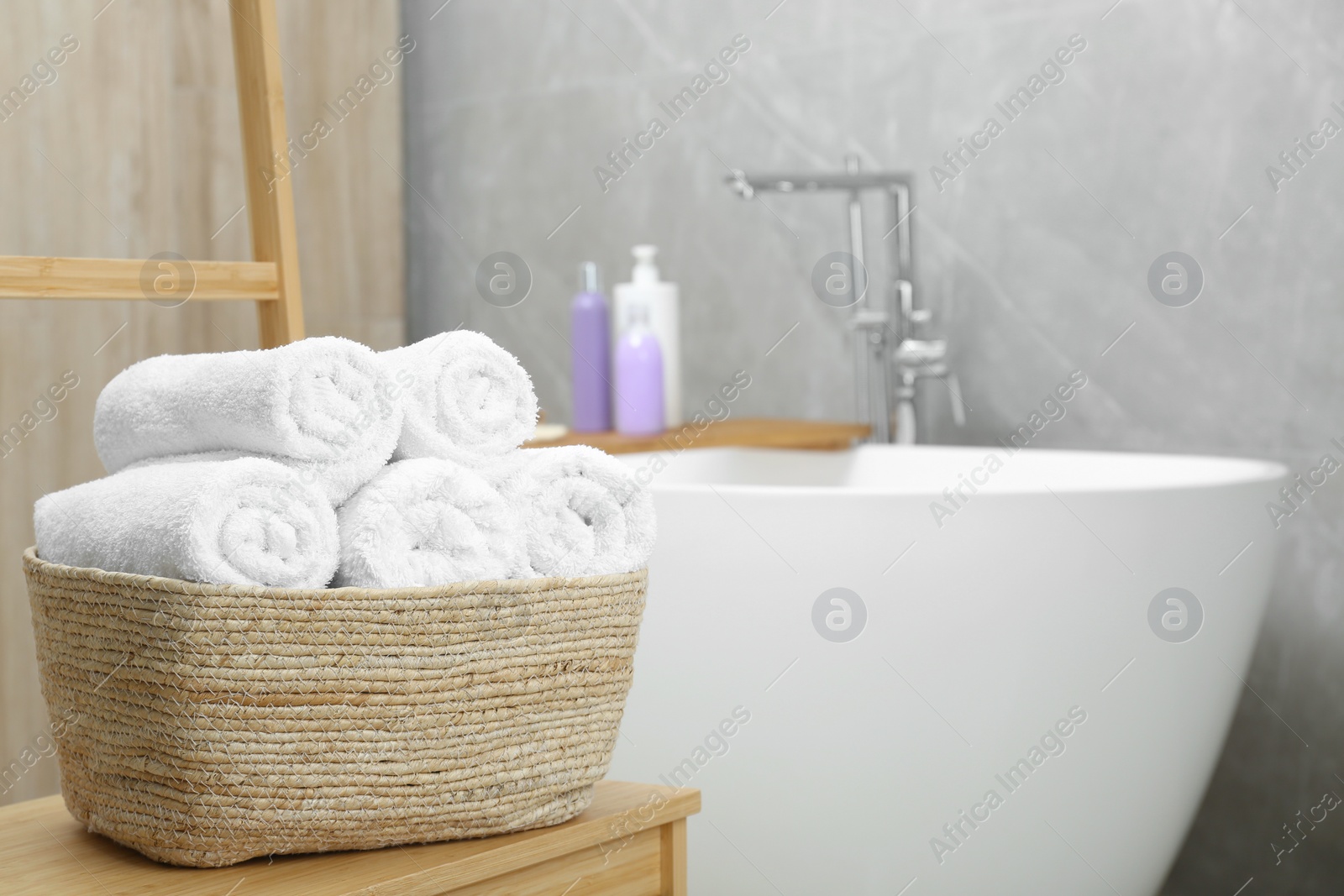 Photo of Wicker basket with rolled bath towels in bathroom, space for text