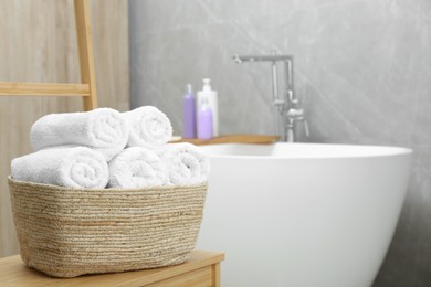 Photo of Wicker basket with rolled bath towels in bathroom, space for text