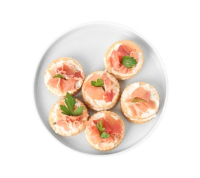 Delicious crackers with cream cheese, prosciutto and parsley on white background, top view