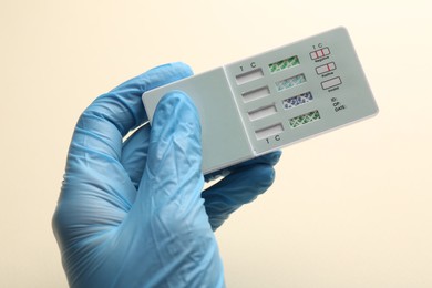 Photo of Doctor holding multi-drug screen test on beige background, closeup
