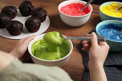 Photo of Woman mixing cream with green food coloring at wooden table, closeup