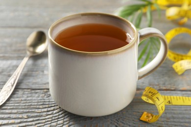 Photo of Cup of herbal diet tea and measuring tape on grey wooden table, closeup. Weight loss concept