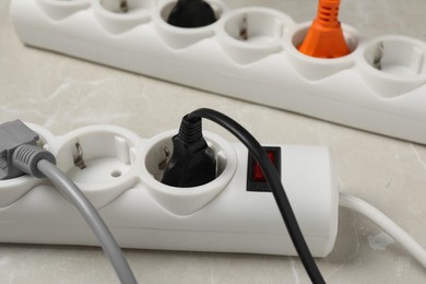Photo of Power strip with extension cords on grey marble table, closeup. Electrician's equipment