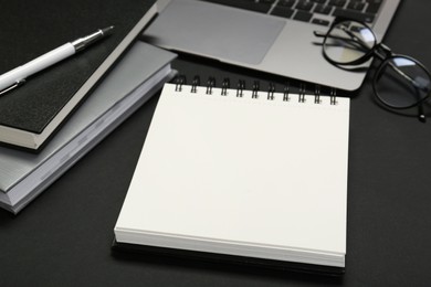 Photo of Notebooks, laptop, glasses and pen on black table