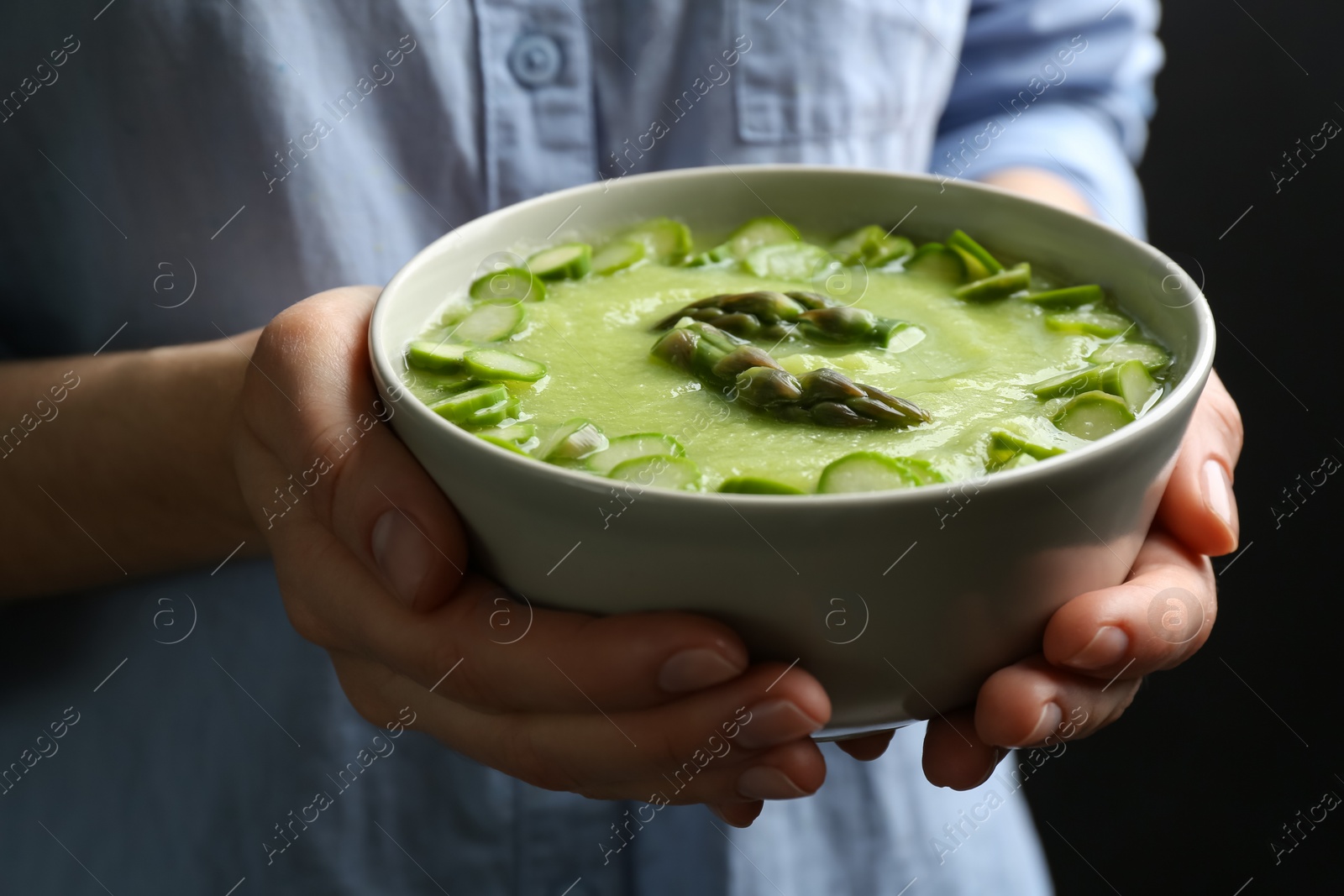 Photo of Woman holding bowl with delicious asparagus soup on black background, closeup