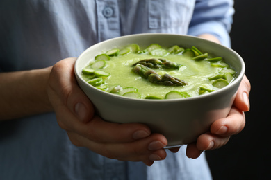 Photo of Woman holding bowl with delicious asparagus soup on black background, closeup