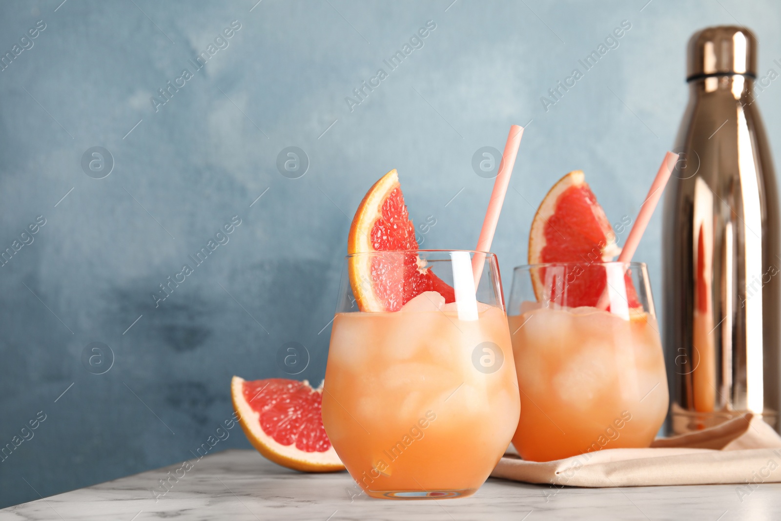 Photo of Glasses of grapefruit cocktails served on table against color background. Space for text