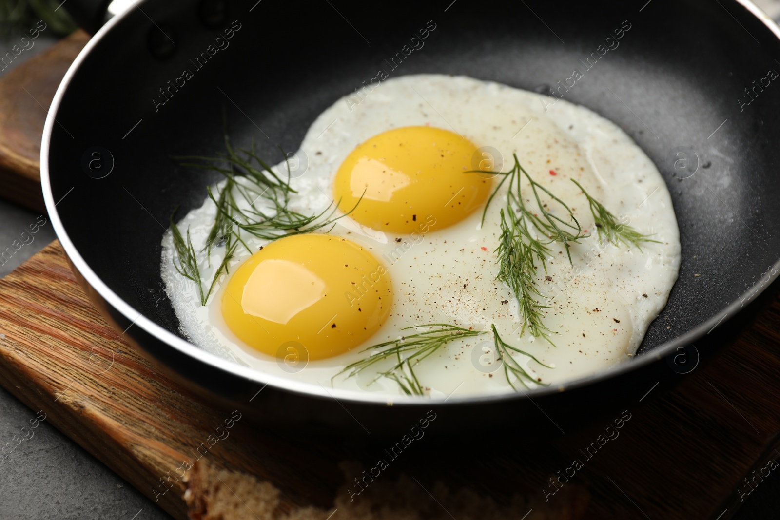 Photo of Frying pan with tasty cooked eggs and dill on black table, closeup