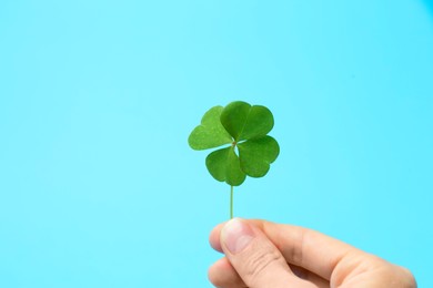 Photo of Woman holding beautiful green four leaf clover on light blue background, closeup