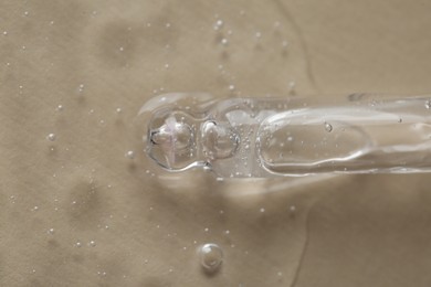 Photo of Pipette with cosmetic serum on beige background, macro view