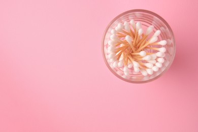 Photo of Glass with clean cotton buds on pink background, top view. Space for text
