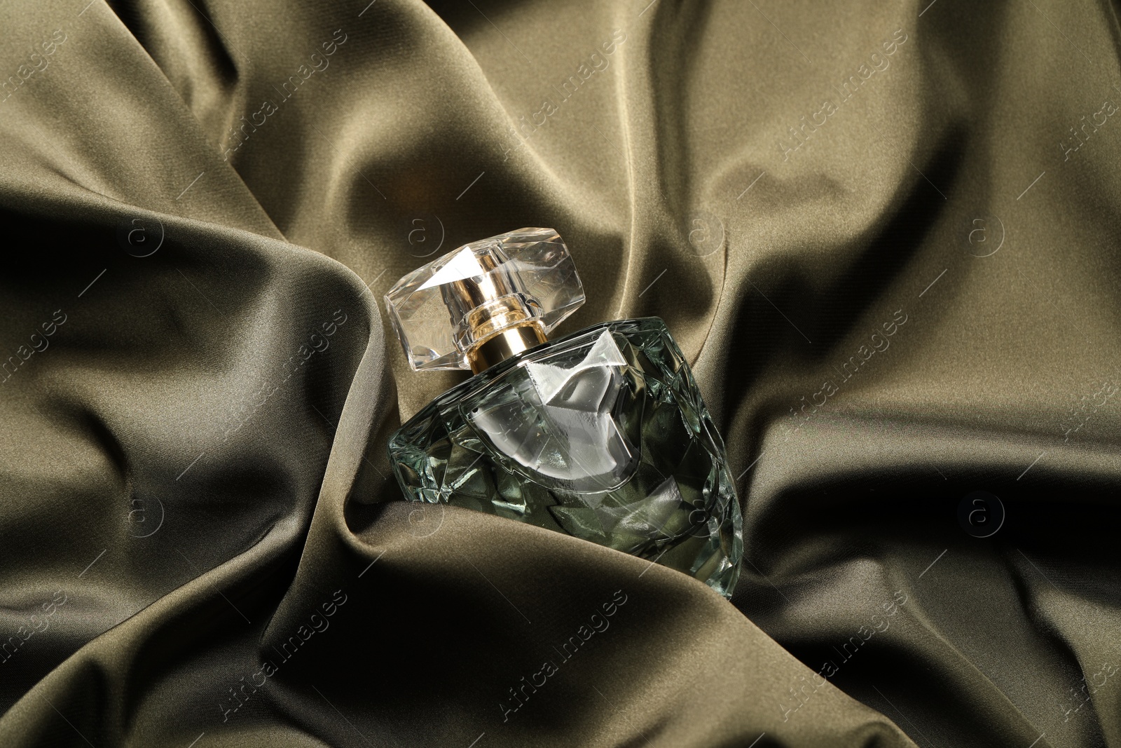 Photo of Luxury perfume in bottle on dark silk fabric, top view