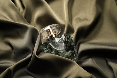 Photo of Luxury perfume in bottle on dark silk fabric, top view