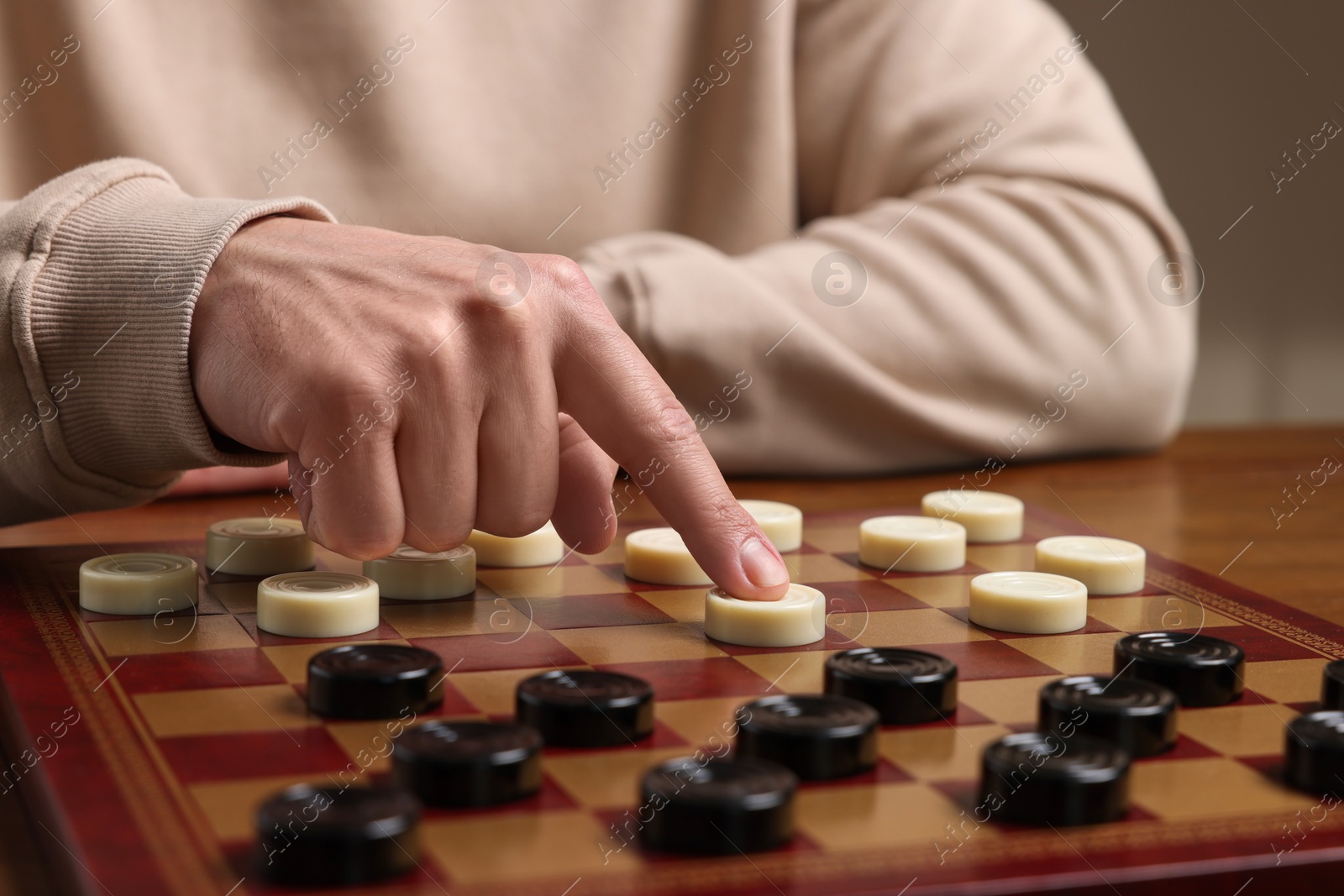 Photo of Playing checkers. Man thinking about next move at wooden table, closeup