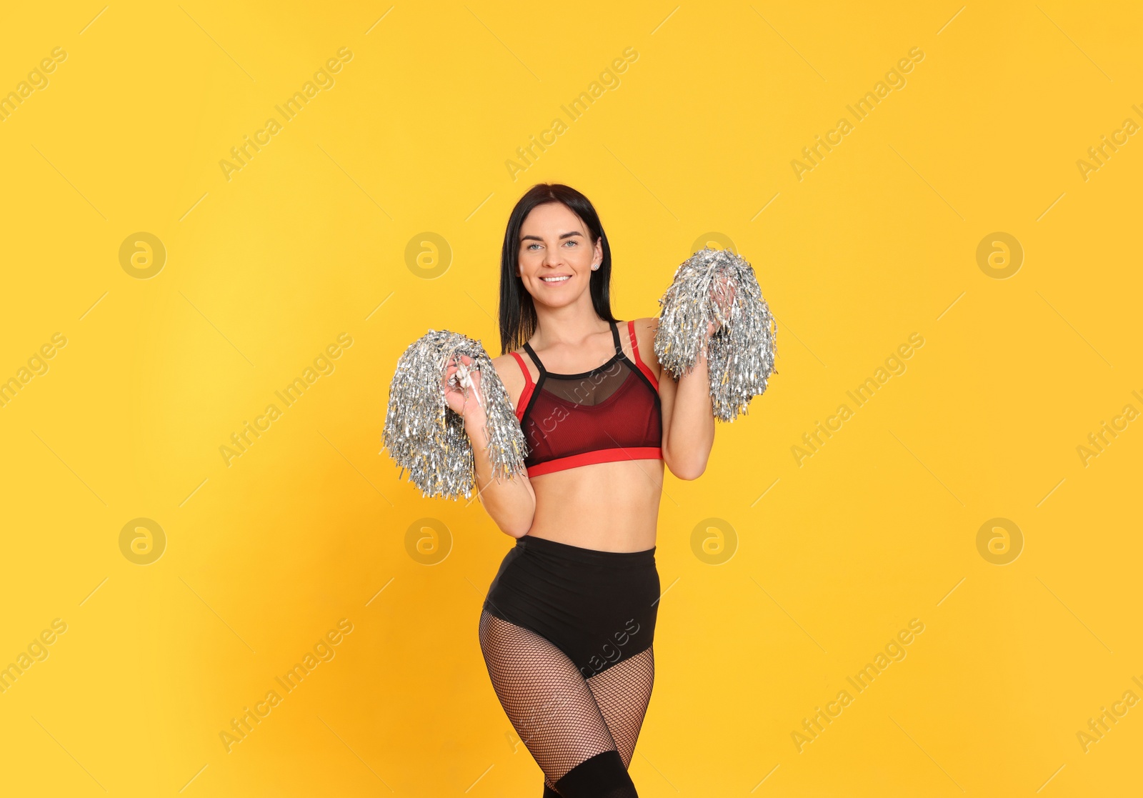 Photo of Beautiful cheerleader in costume holding pom poms on yellow background