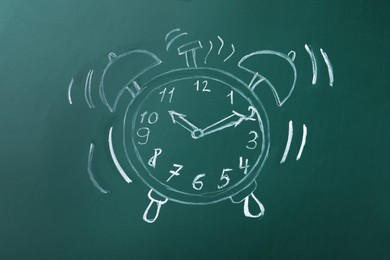 Photo of Drawn alarm clock on green chalkboard. School time