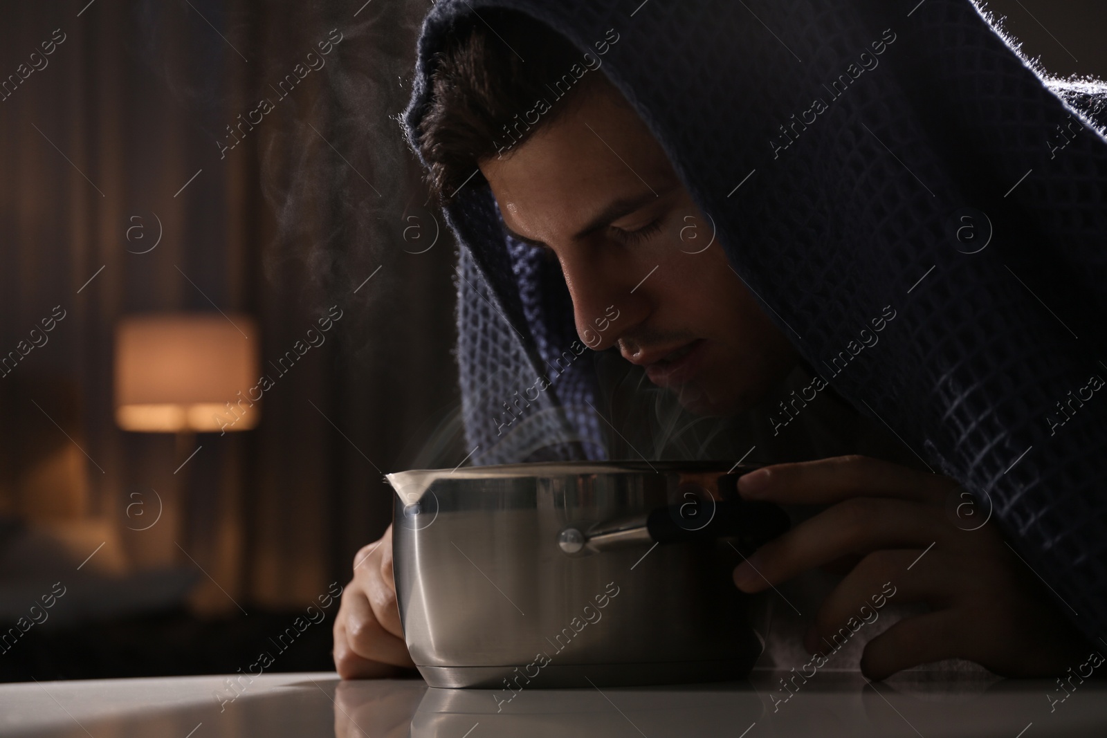 Photo of Man with plaid doing inhalation above saucepot at table indoors