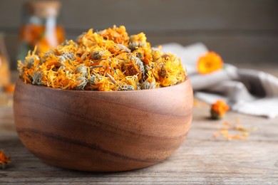 Photo of Bowl of dry calendula flowers on wooden table, closeup