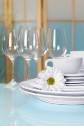 Set of clean dishware and flower on light blue table, closeup