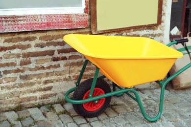 Bright yellow wheelbarrow near brick wall outdoors