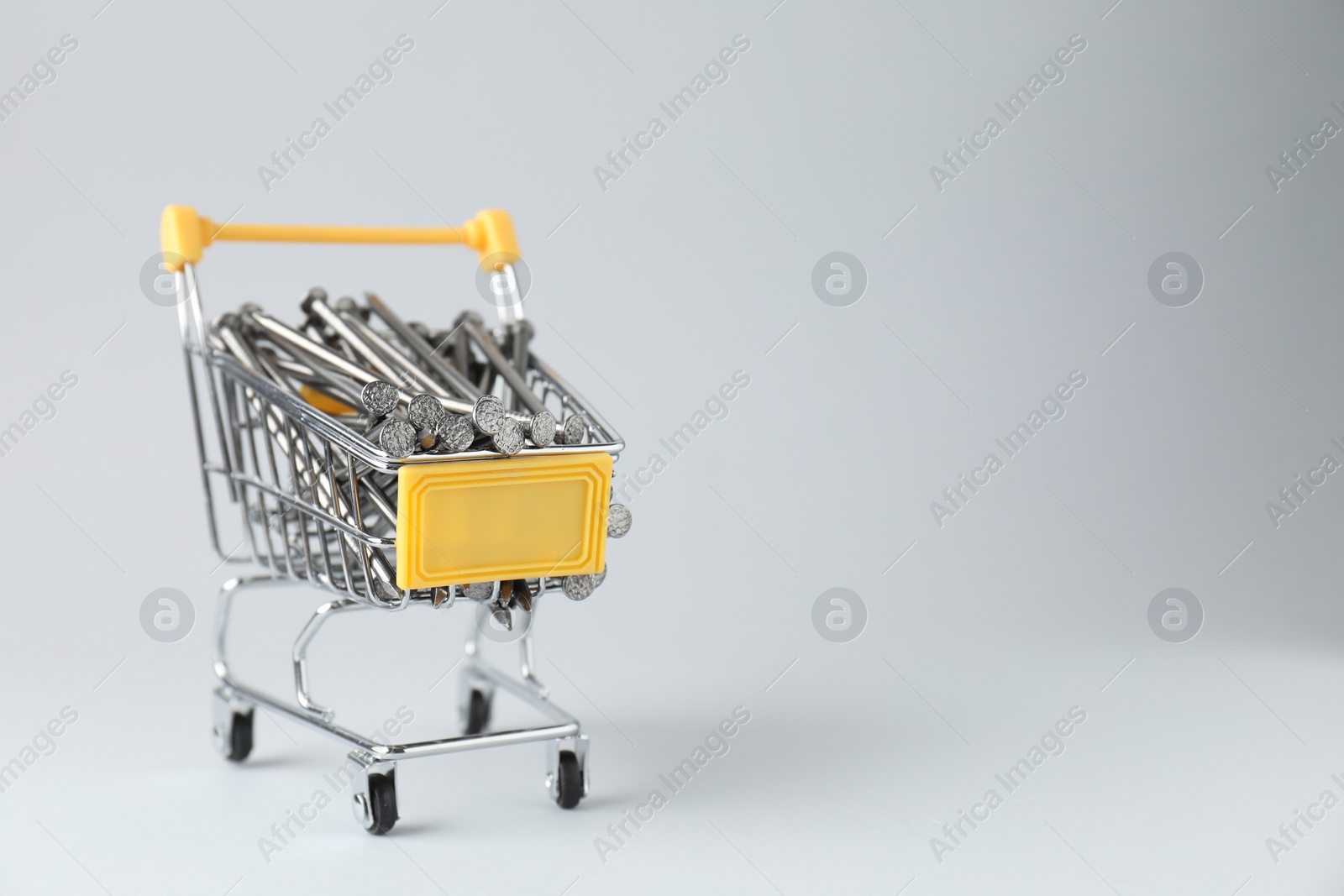 Photo of Metal nails in shopping cart on light grey background, space for text