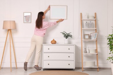 Woman hanging picture frame on white wall at home