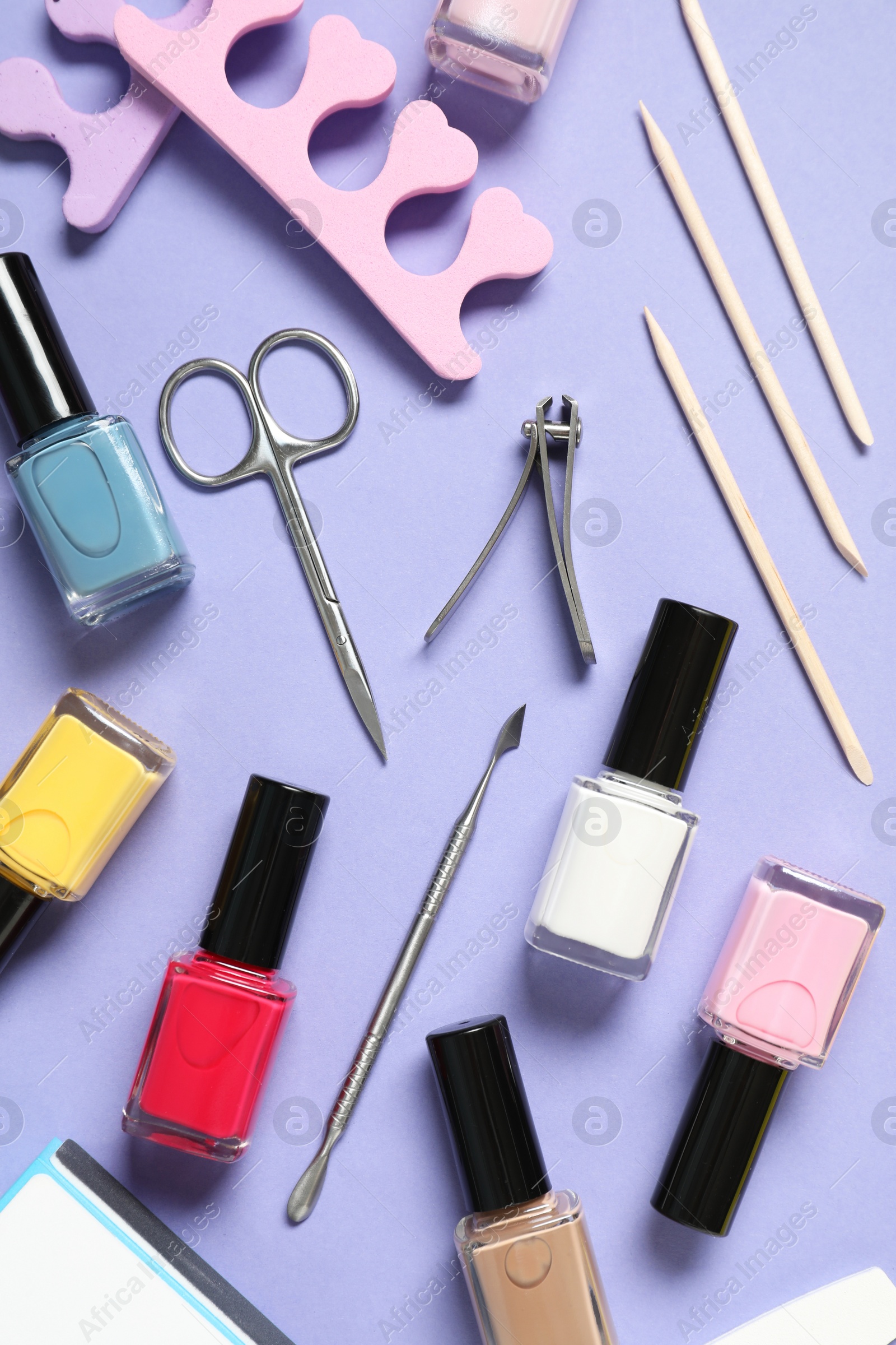 Photo of Nail polishes and set of pedicure tools on lilac background, flat lay