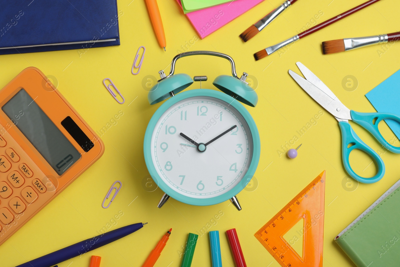 Photo of Flat lay composition with alarm clock and different stationery on yellow background. School time