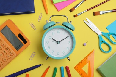 Photo of Flat lay composition with alarm clock and different stationery on yellow background. School time