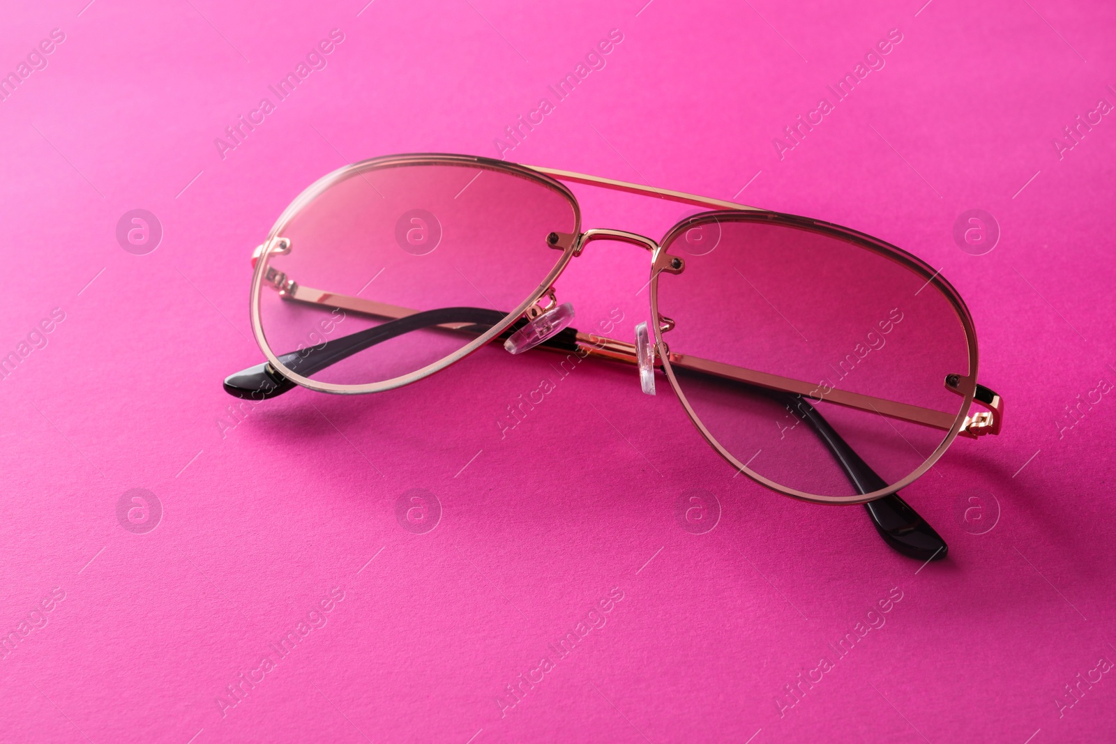 Photo of New stylish sunglasses on pink background, closeup. Fashionable accessory