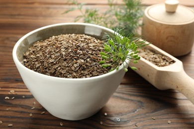 Photo of Bowl of dry seeds, scoop and fresh dill on wooden table, closeup