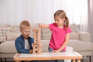 Photo of Little girl and boy playing with wooden tower at table indoors. Children's toy