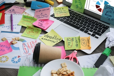 Photo of Laptop, notes and office stationery in mess on desk. Overwhelmed with work