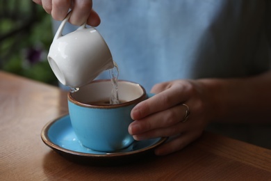 Photo of Woman adding water to fresh aromatic coffee at table, closeup