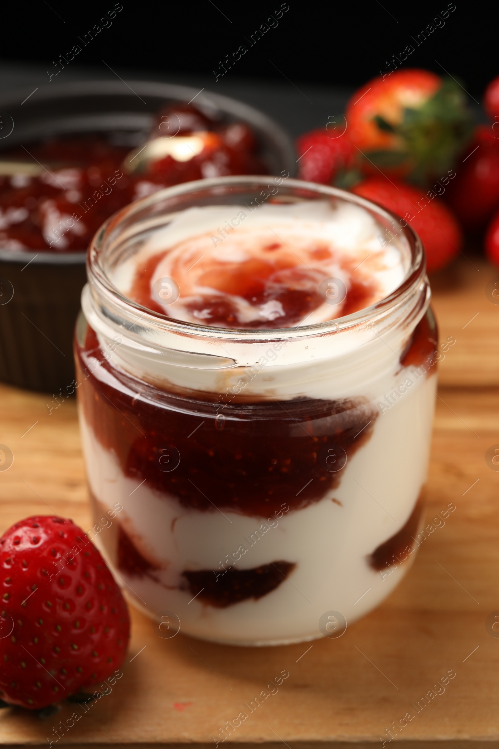 Photo of Tasty yoghurt with jam and strawberries on wooden board, closeup