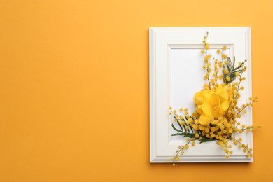 Photo of Beautiful floral composition with mimosa flowers and frame on orange background, top view. Space for text