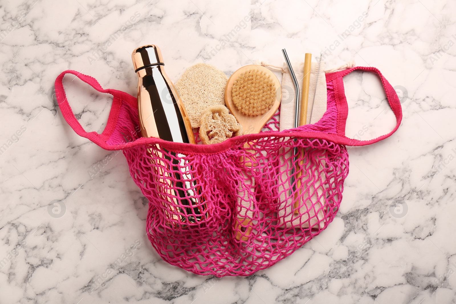 Photo of Net bag with different items on white marble table, top view. Conscious consumption