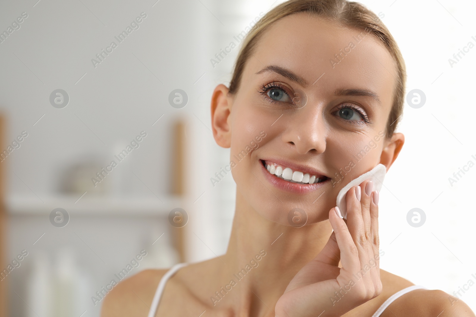 Photo of Smiling woman removing makeup with cotton pad indoors, closeup. Space for text