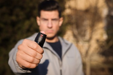 Photo of Man using pepper spray outdoors, focus on hand. Space for text