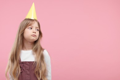 Photo of Bored little girl in party hat on pink background. Space for text