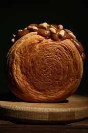 Photo of Round croissant with chocolate paste and nuts on wooden table, closeup. Tasty puff pastry
