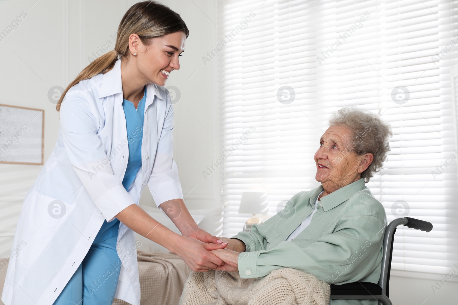 Photo of Young caregiver assisting senior woman in wheelchair indoors. Home health care service