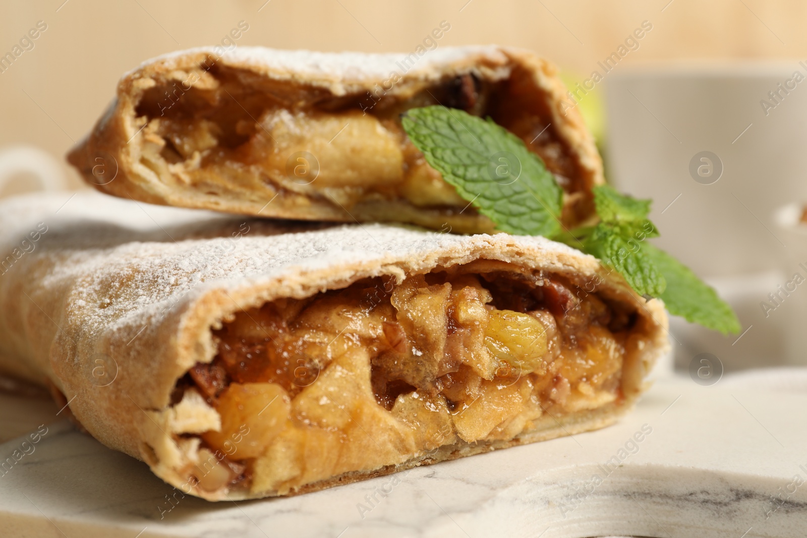 Photo of Delicious strudel with apples, nuts and raisins on marble board, closeup