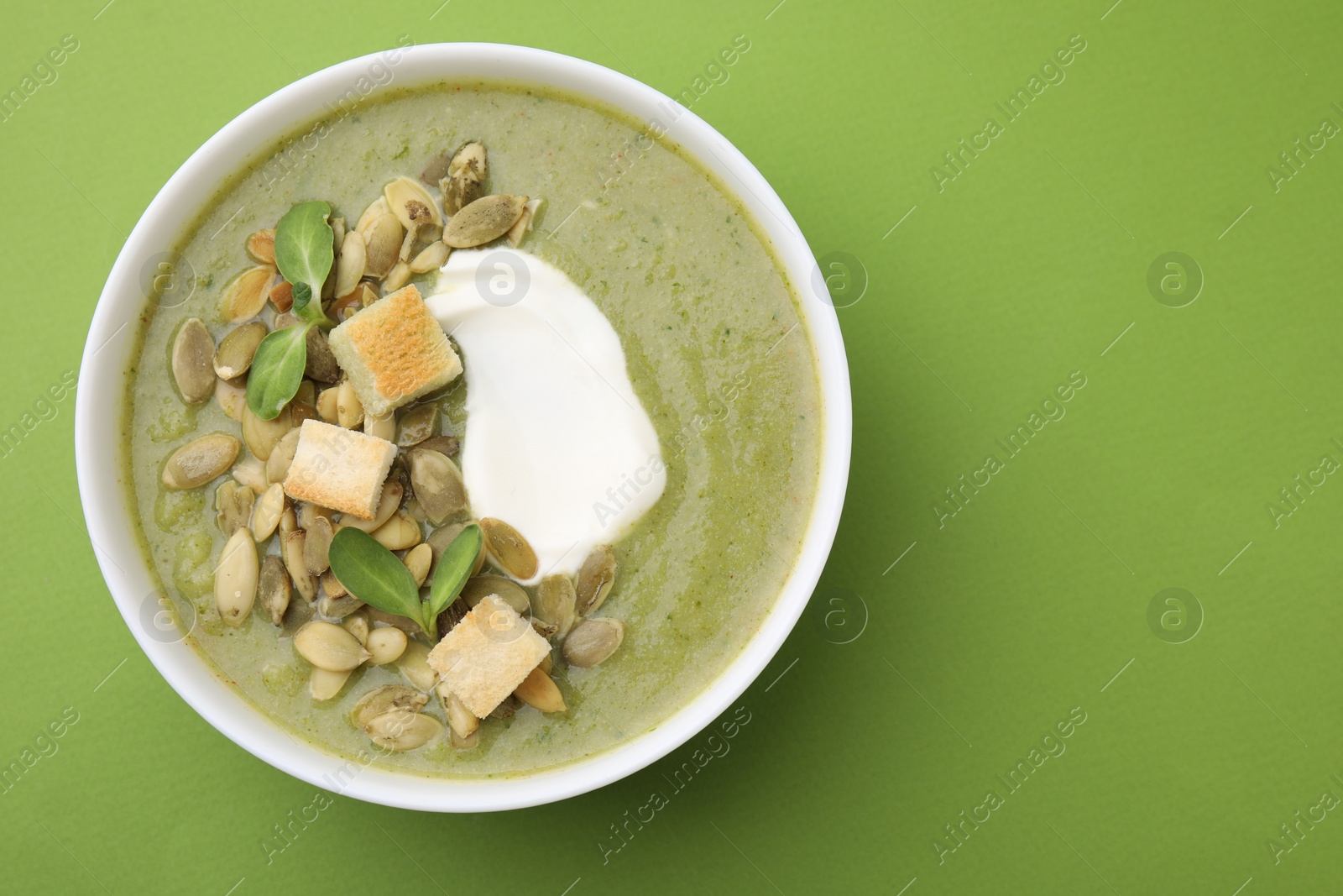 Photo of Delicious broccoli cream soup with croutons, sour cream and pumpkin seeds on green background, top view. Space for text