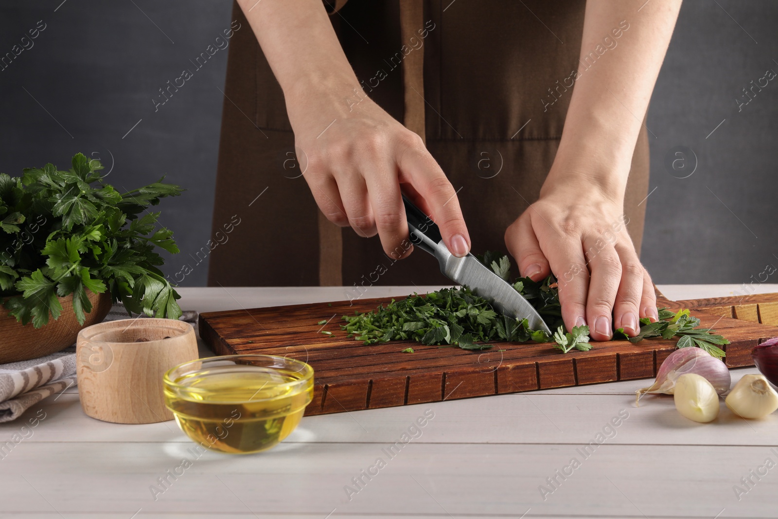 Photo of Woman cutting fresh parsley at white wooden table, closeup