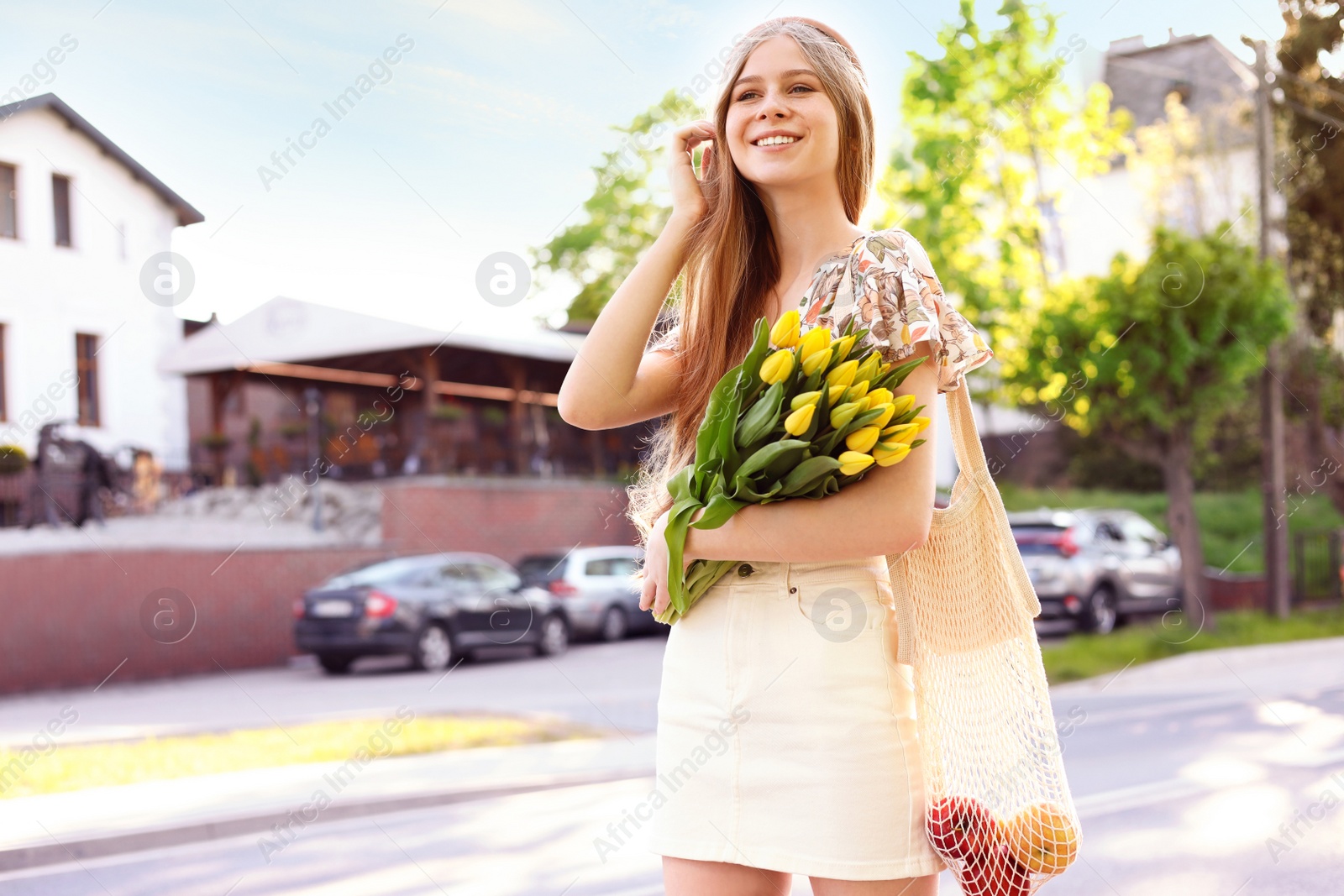 Photo of Beautiful teenage girl with bouquet of yellow tulips on city street, space for text