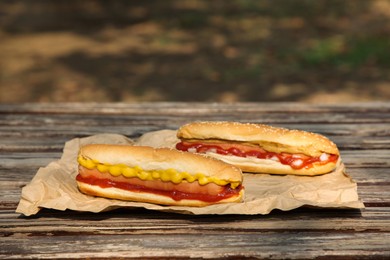 Photo of Fresh delicious hot dogs with sauces on wooden surface outdoors