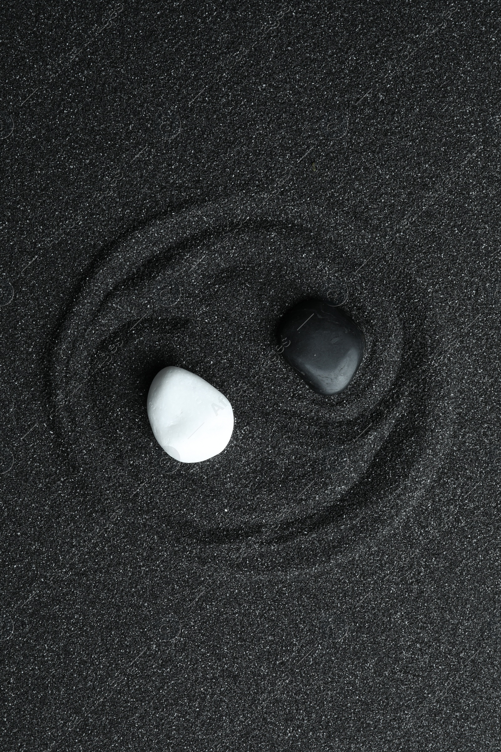 Photo of Yin Yang symbol made with stones on black sand, top view. Zen concept
