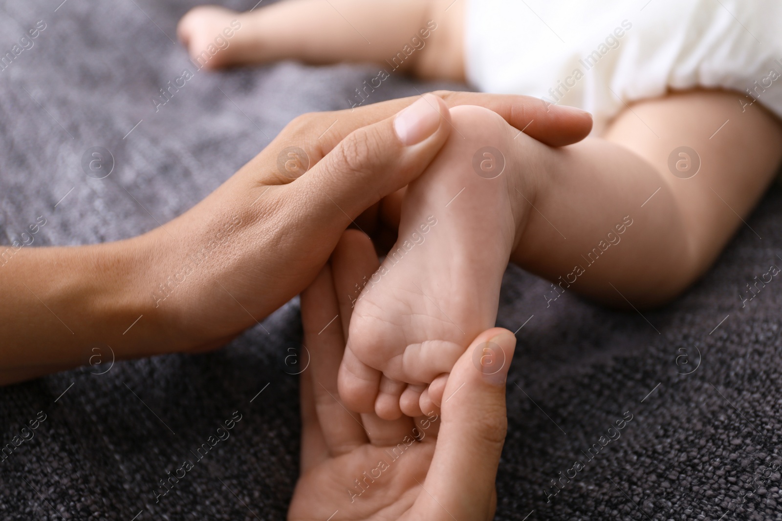 Photo of Woman massaging cute little baby on blanket, closeup